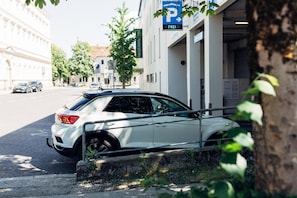 En hvid bil parkeret foran en bygning med et parkeringsskilt.