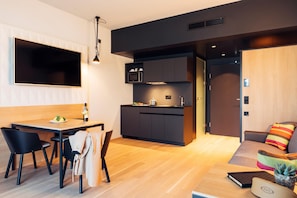 A modern kitchen with dark cabinetry, a flat-screen TV, and a dining area with a wooden table and chairs. - Harry's Home Steyr Hotel (Alberndorf in der Riedmark)