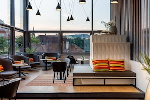 A modern interior with a seating area, tables, and large windows offering a view of the cityscape. - Harry's Home Steyr Hotel (Alberndorf in der Riedmark)