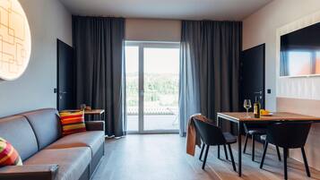 Een moderne hotelkamer met een bank, eettafel, stoelen, een televisie en een glazen schuifdeur die leidt naar een buitenruimte.