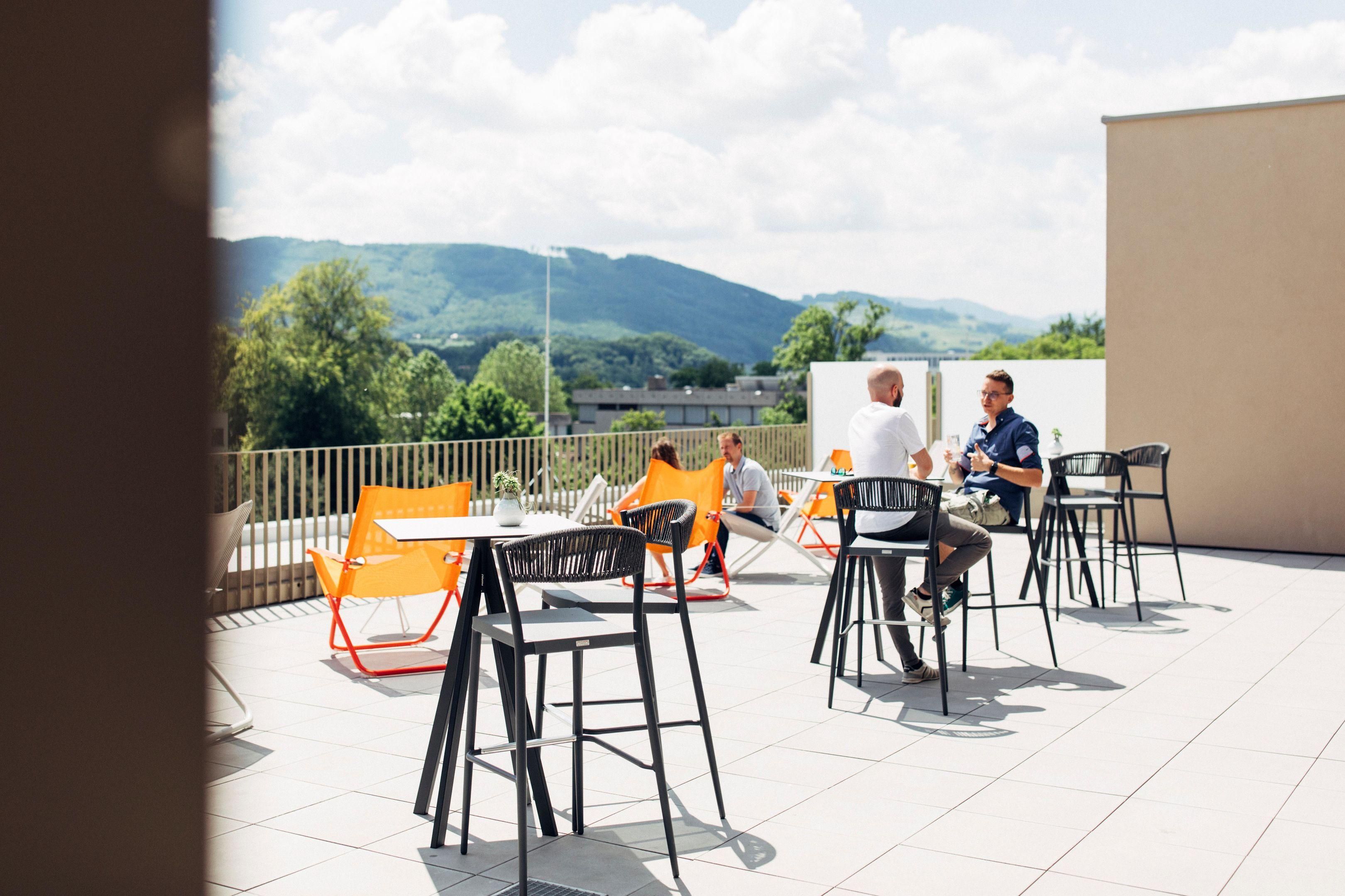 Eine Terrass mit Tischen und Stühlen, Blick auf die Landschaft, und ein Gebäude im Hintergrund.
