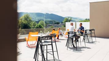 Eine Terrass mit Tischen und Stühlen, Blick auf die Landschaft, und ein Gebäude im Hintergrund.