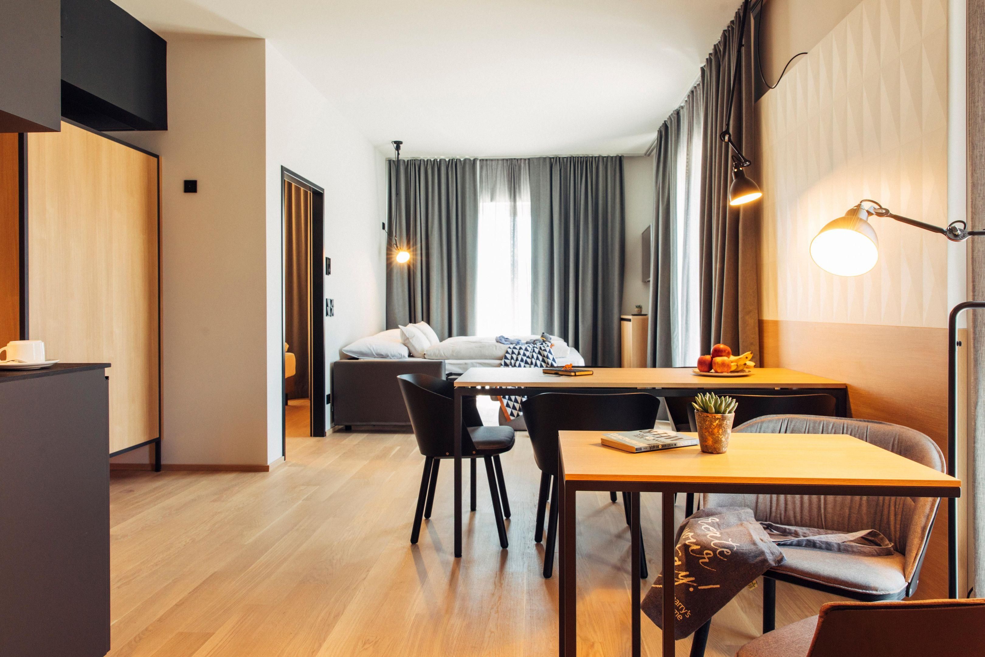 Ein modernes Hotelzimmer mit Essbereich, einer Couch, einem Schreibtisch und einer Lampe.