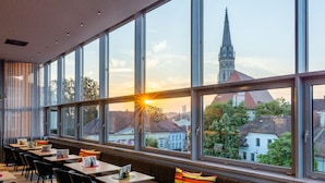 Un restaurante con amplios ventanales, vistas a la aguja de una iglesia y un atardecer.