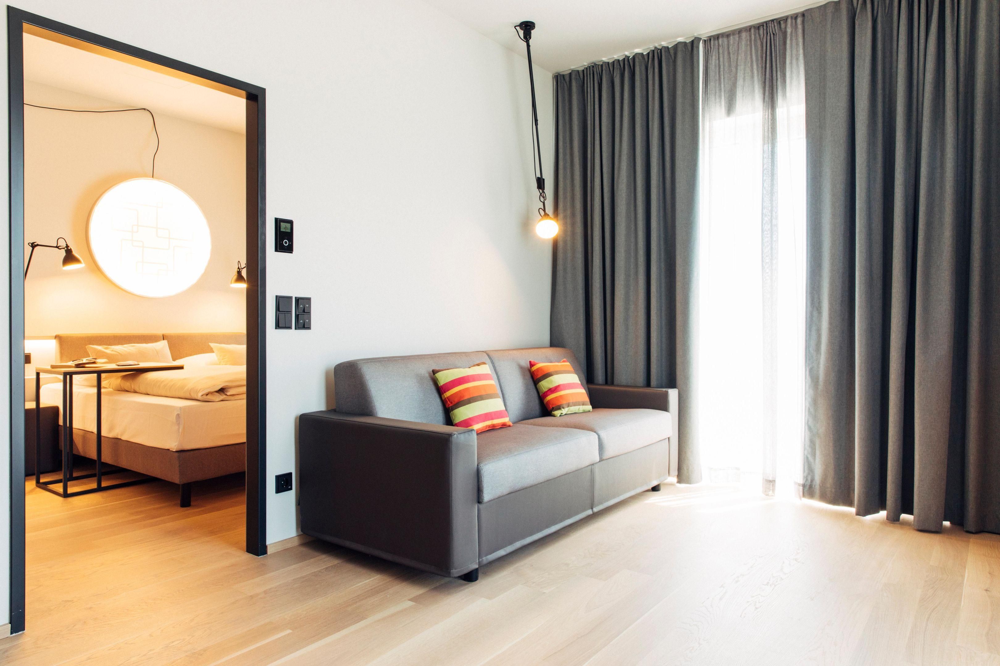Ein modernes Wohnzimmer mit einem grauen Sofa, einer runden Lampe und Blick durch eine Tür.