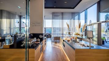 A modern hotel lobby with a central counter, large windows, and a view of the outdoors.