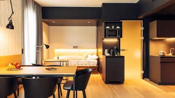 A modern hotel room with a dining area, kitchenette, and a bed with a headboard.