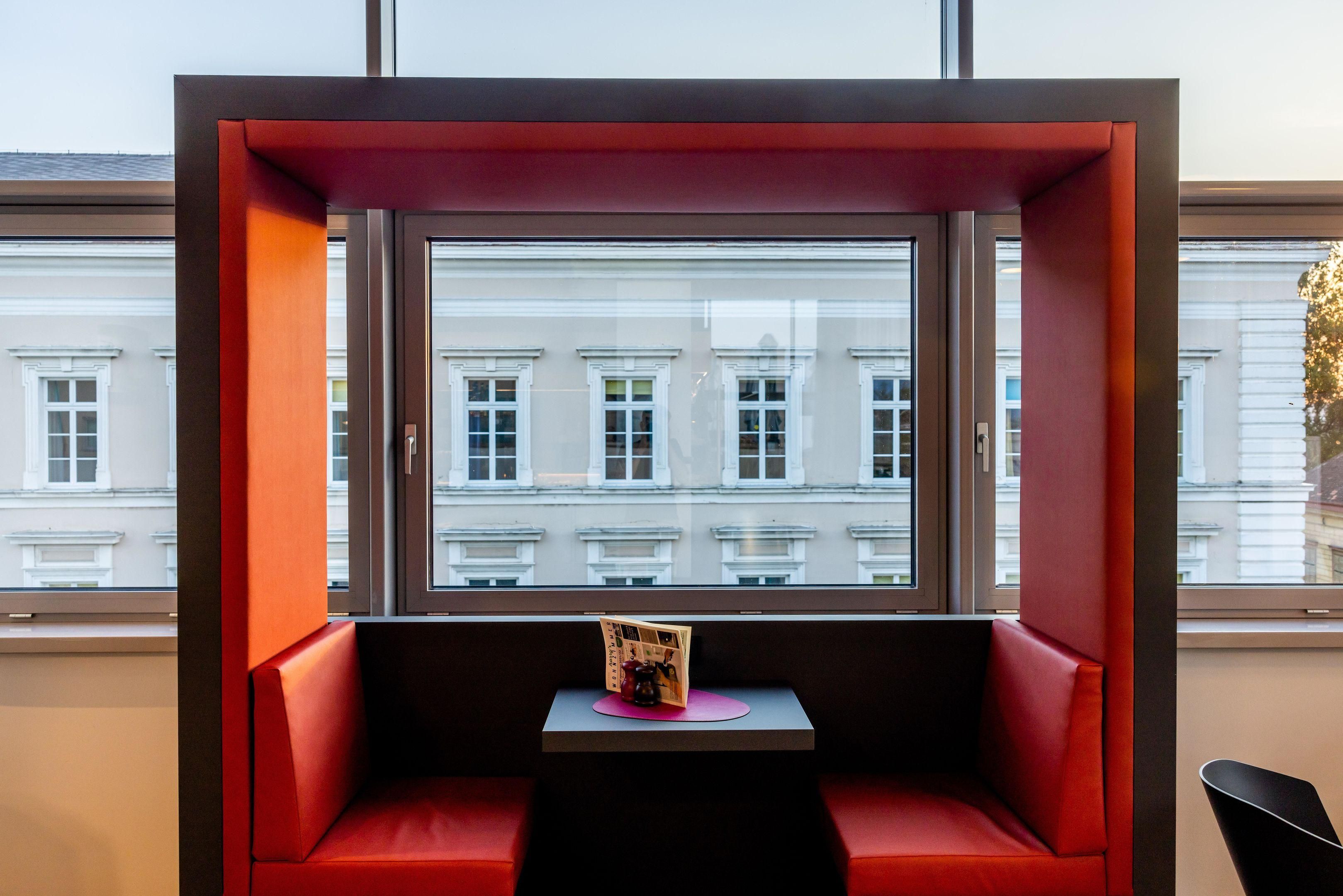 Ein rotes Sitzarrangement mit kleinem Tisch und einer Zeitschrift, mit Blick auf eine Reihe weißer Gebäude.