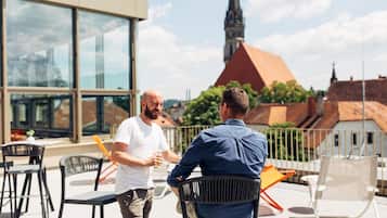 Two men conversing on a rooftop terrace with a church steeple in the background.