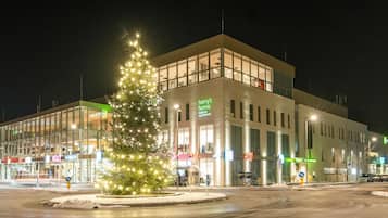 Un edificio moderno con un árbol de Navidad en primer plano, ventanas amplias y varios carteles que indican hoteles y apartamentos.