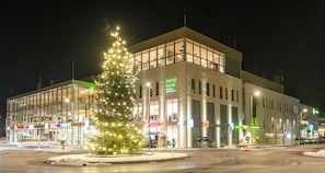 A modern building with a Christmas tree in front, large windows, and various signs indicating hotels and apartments.