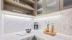 Una cocina moderna con encimeras de mármol, una cafetera, un bol, una cesta de pan y una planta.