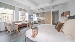 Una habitación de hotel moderna con una cama grande, zona de estar, kitchenette y vistas a la ciudad.