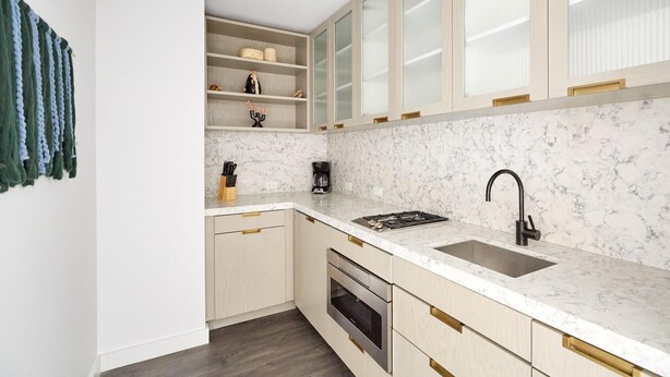 Una cocina moderna con encimeras de mármol, horno empotrado, pileta con grifo negro y muebles de color claro.
