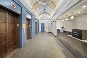 A hotel lobby with a reception desk, a digital clock, and a patterned ceiling. - Sonder City Hall Park (New York)
