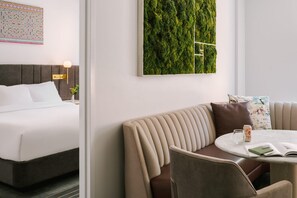 A hotel room with a bed, a sofa, a small table with a drink, and a wall-mounted green wall. - Sonder City Hall Park (New York)