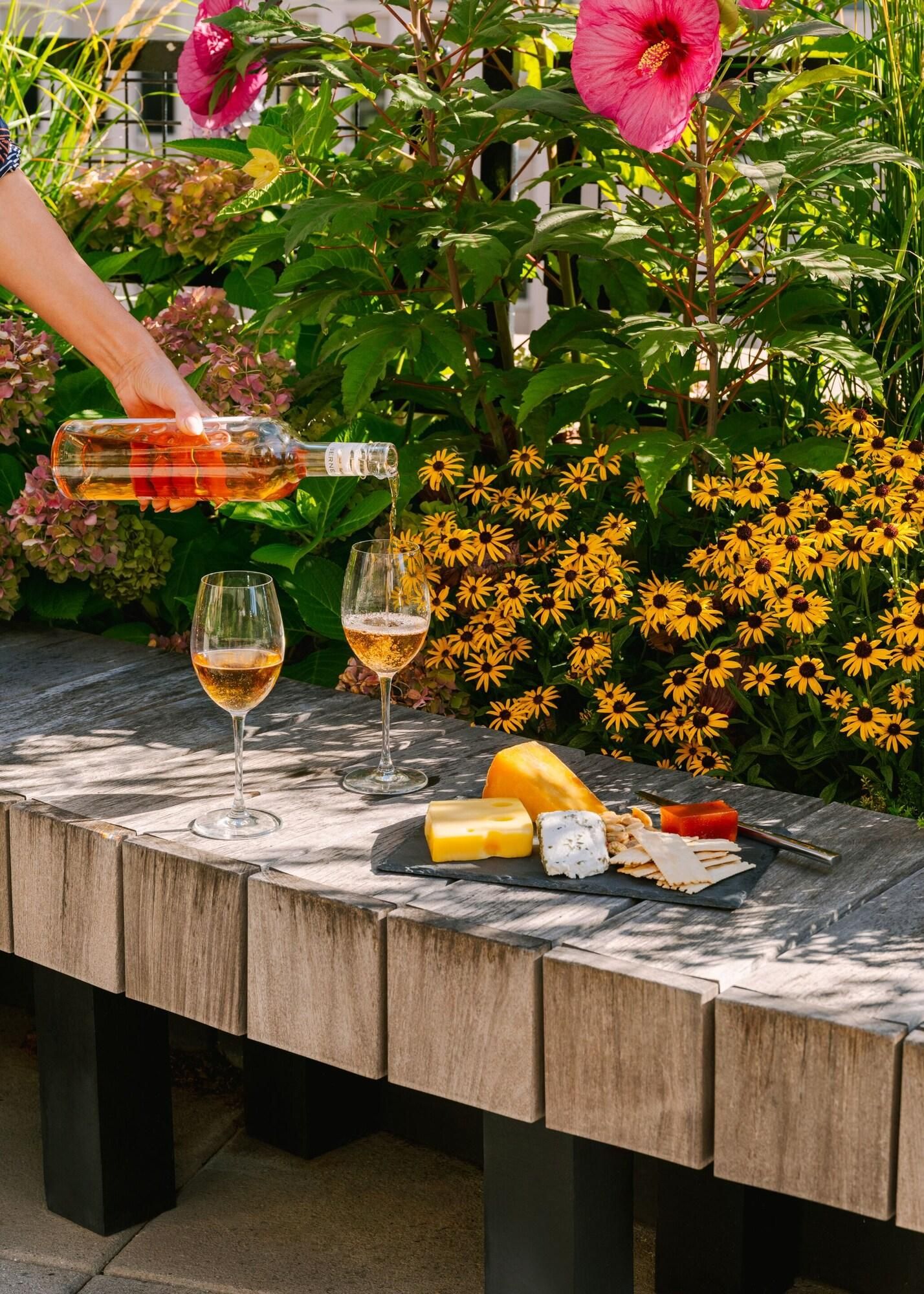 A table set outdoors with wine glasses, cheese, and a bottle of wine.