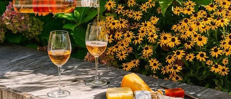Una mesa al aire libre con copas de vino, queso y una botella de vino.
