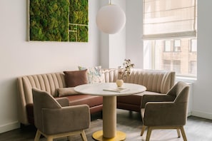 Un salon moderne avec un canapé d’angle, deux fauteuils, une table basse ronde, un luminaire suspendu et une vue sur la ville à travers une grande fenêtre.