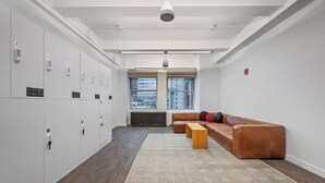Un espacio de oficina moderno con taquillas, un sofá de cuero, un banco de madera y ventanas amplias.