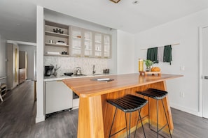 A modern kitchen with a wooden island, bar stools, and a view into the living area.