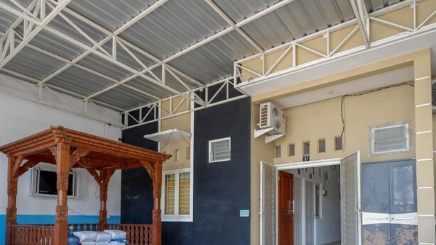 Una habitación con un banco de madera, una mesa, un techo con vigas de metal y una puerta que da a otra habitación.