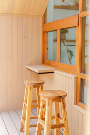 Una terraza de madera con dos taburetes de madera y una ventana que ofrece vistas a la vegetación.