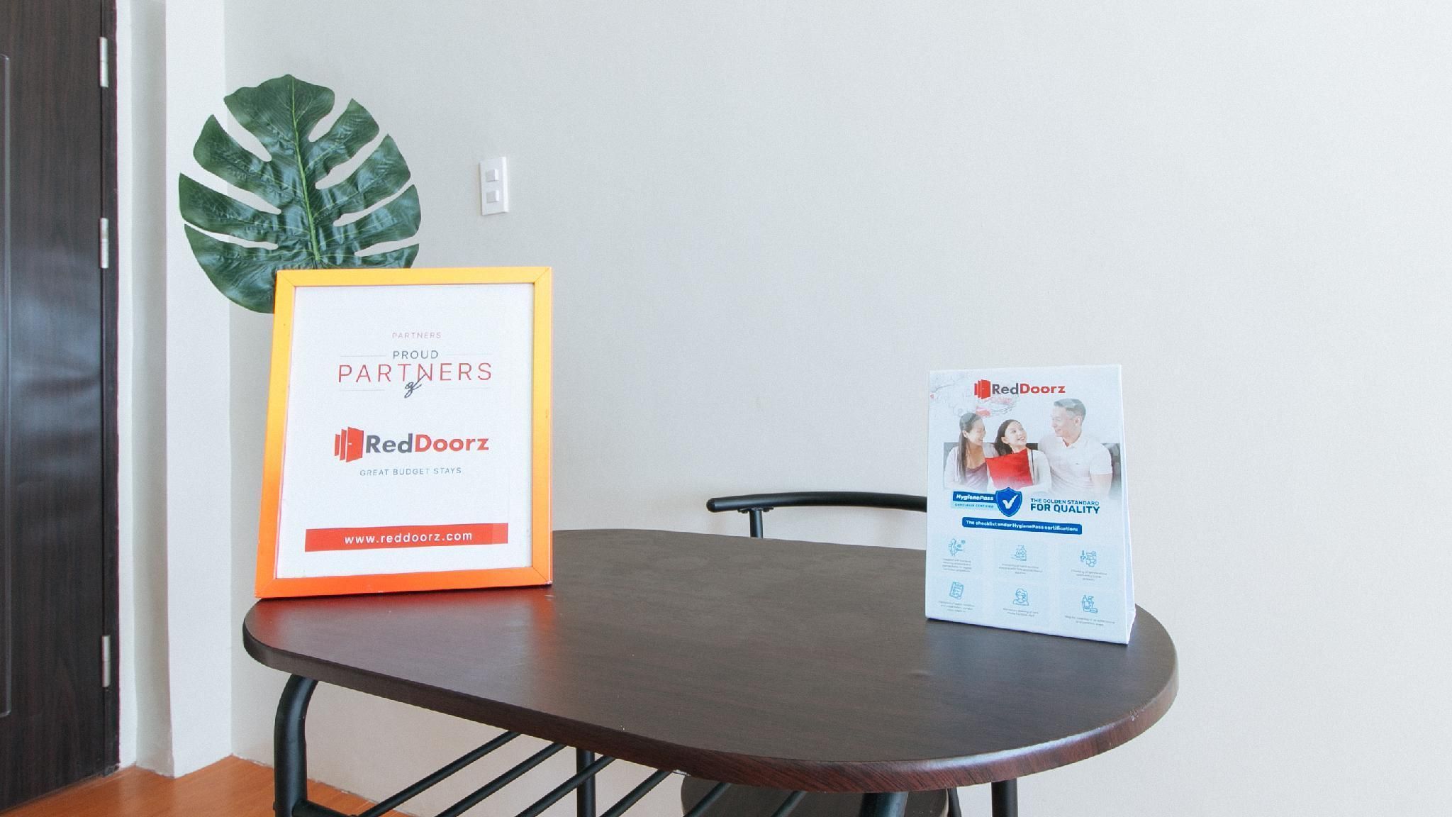 A framed certificate on a table with a RedDoorz sign, a potted plant, and a chair.
