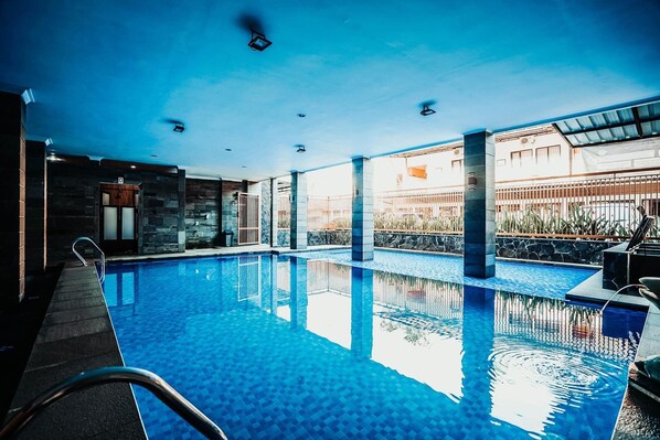 A swimming pool with clear water, a sunroof, and a stone wall. - The Priangan Hotel Sudirman (Ciamis)