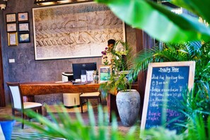 A reception desk with a computer, a chalkboard menu, and a large wall mural. - Rivertree Villa and Resort (Kampot)