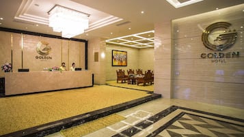 A hotel reception area with a marble counter, a chandelier, and a conference room with wooden furniture.