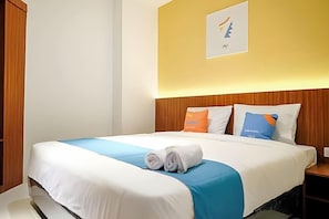 A hotel room with a bed, a wall-mounted artwork, and a wooden headboard. - Sans Hotel Roxy Jakarta (Jakarta)