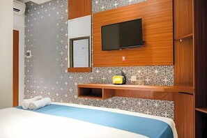 Hotellihuone, jossa on sänky, seinälle asennettu televisio ja pieni hylly, jonka päällä on radio.