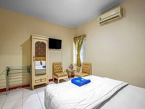A hotel room with a bed, a wardrobe, a television, a chair, a small table, and an air conditioning unit. - Hotel Cempaka Sari (Jakarta)