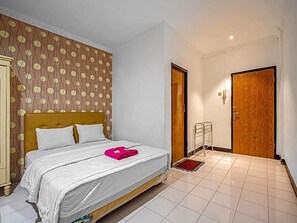 A hotel room with a bed, a wooden door, a wardrobe, and a patterned wall. - Hotel Cempaka Sari (Jakarta)