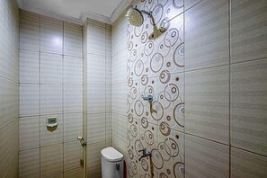 A bathroom with tiled walls, a toilet, a shower with a handheld showerhead, and a soap dispenser. - Hotel Cempaka Sari (Jakarta)