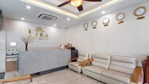 A reception area with a marble counter, a sofa, a ceiling fan, and clocks indicating different time zones. - Lara Hotel (Long Xuyen)