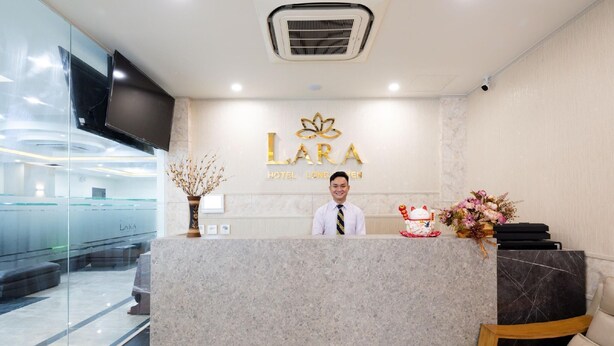 A hotel reception desk with a modern design, a receptionist, and a logo for 'LARA HOTEL LONGAVEN'. - Lara Hotel (Long Xuyen)