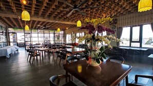 A spacious dining area with wooden tables and chairs, large windows, and hanging pendant lights. - Lara Hotel (Long Xuyen)
