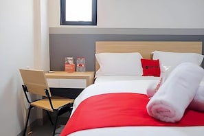 Hotellihuone, jossa on sänky, työpöytä, tuoli ja ikkuna.