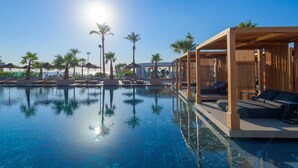 A pool with clear water, surrounded by lounge chairs and palm trees. - Ammades All Suites Beach Hotel - Adults Only (Rhodes)