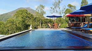 A pool area with lounge chairs and umbrellas, surrounded by greenery and a mountain view. - Bunbulan Cottage Lake View (Kintamani)