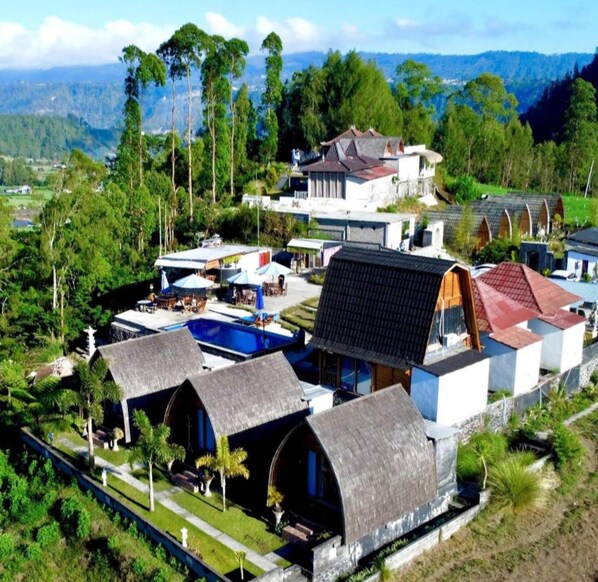 A resort with multiple bungalow-style accommodations, a swimming pool, and a view of the surrounding landscape.