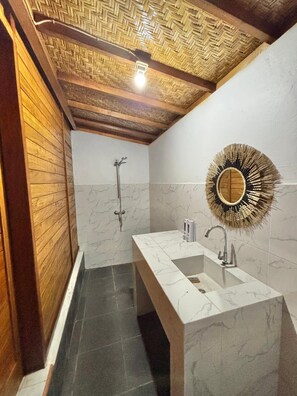 A bathroom with a wooden ceiling, a shower, a sink with a mirror, and marble tiles.