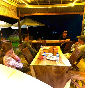 Un espace extérieur aménagé pour les repas, avec des tables et des chaises en bois, des parasols et une vue sur le ciel nocturne.