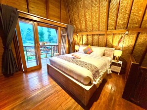 A wooden-framed bedroom with a large bed, two bedside tables with lamps, and a view through a sliding glass door.