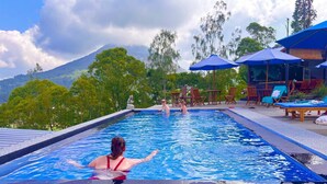 A swimming pool with a view of mountains, surrounded by lounge chairs and umbrellas. - Bunbulan Cottage Lake View (Kintamani)