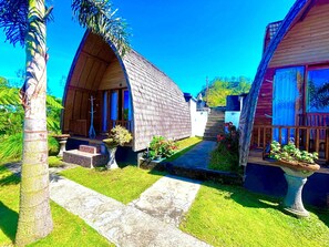 A bungalow-style house with a thatched roof, surrounded by lush greenery and a clear blue sky.