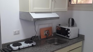 A compact kitchen with a microwave, toaster, and kettle on the counter, a small sink, and a window above the sink. - Lilly Rooms And Studios (Hurghada)