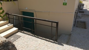 A building with a green door, a number '7' sign, a metal railing, and a stone-paved ground. - Lilly Rooms And Studios (Hurghada)